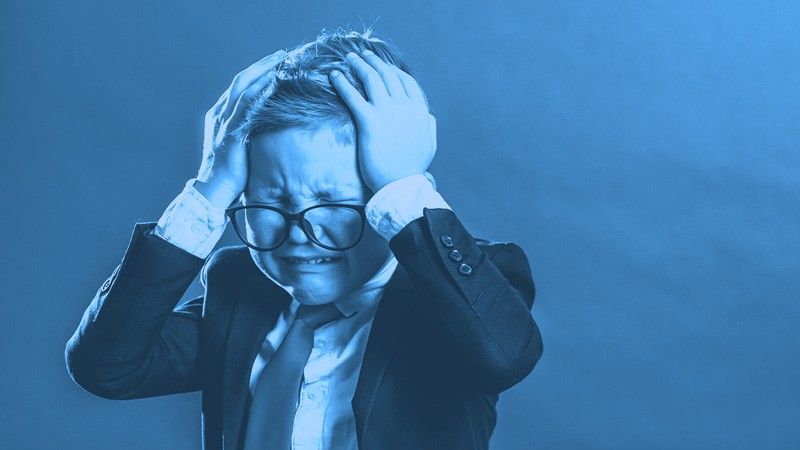 A frustrated boy in a suit and glasses clutching his head in distress, shown with a blue monochromatic filter.