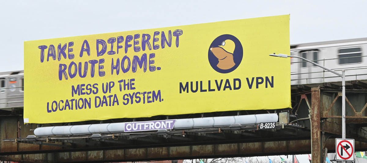 Yellow Mullvad VPN billboard by a passing train: TAKE A DIFFERENT ROUTE HOME. MESS UP THE LOCATION DATA SYSTEM. MULLVAD VPN.