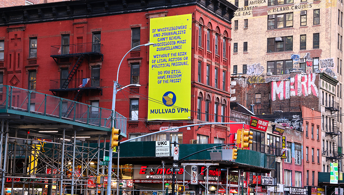 Yellow Mullvad VPN billboard on a city building: IF WHISTLEBLOWERS AND JOURNALISTS CAN'T REVEAL UNDISCLOSED MASS SURVEILLANCE WITHOUT THE RISK OF LEGAL ACTION OR POLITICAL PRESSURE, DO YOU STILL HAVE FREEDOM OF THE PRESS?