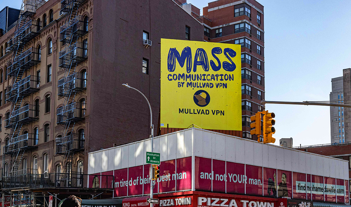 Yellow billboard in NYC reading MASS COMMUNICATION BY MULLVAD VPN with the mole logo above a street corner and Pizza Town restaurant.